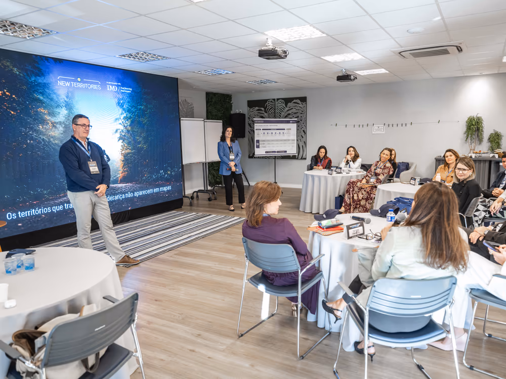 Visão da sala durante uma sessão de co-criação, com participantes nas mesas de trabalho.